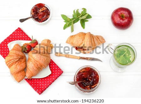 Breakfast with herbal tea, croissants and jam on the white wooden table, top view
