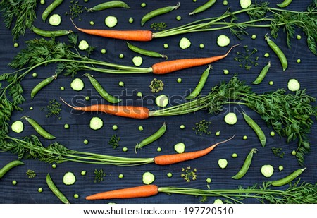 Pattern from carrot, green peas and cucumber on a black wooden background