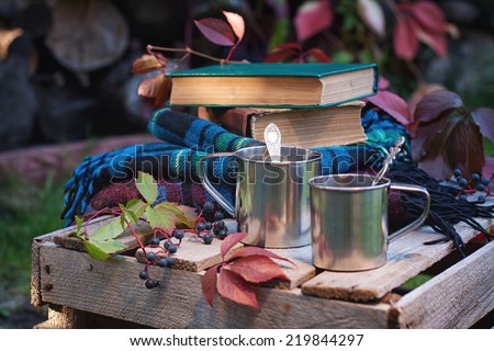 Metallic cups of hot tea, books and plaids on old wooden box