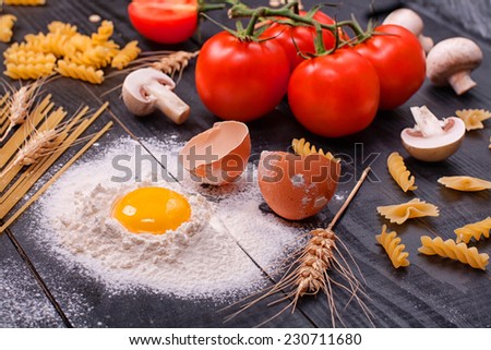Raw pasta, tomatoes,mushrooms, flour and eggs on black wooden table background