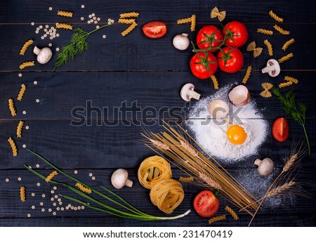 Raw pasta, tomatoes,mushrooms, flour and eggs on black wooden table background, top view and place for your text