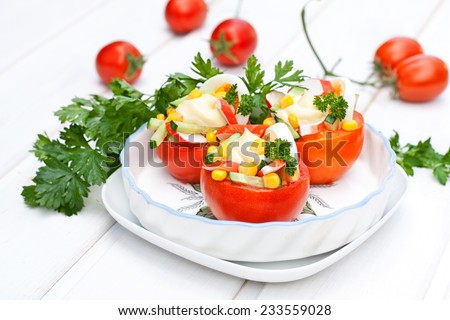Salad with sweet corn and crab sticks, served in a tomatoes, on white background wooden table
