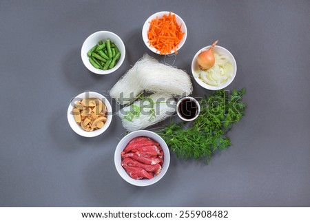 Products for Thai dish of rice pasta, mushrooms, meat, carrots, green beans and soya sauce on a grey background