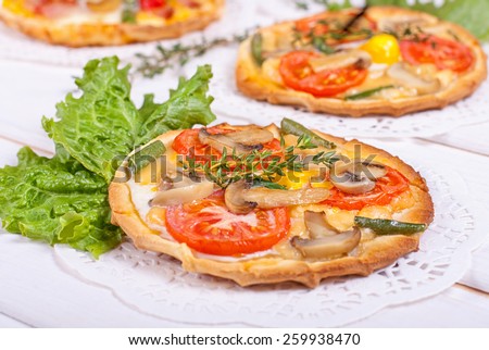 Mini tartlets with champignon, tomato, cheese, quail eggs and black eyed peas on white wooden background