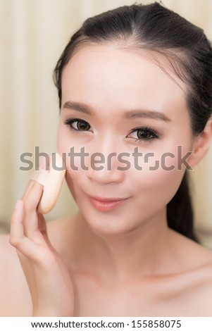 Young Woman applying foundation on face with Powder puff,model is a asian beauty