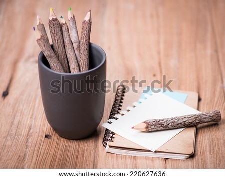 color pencil made of branches in cup and note book on wood background