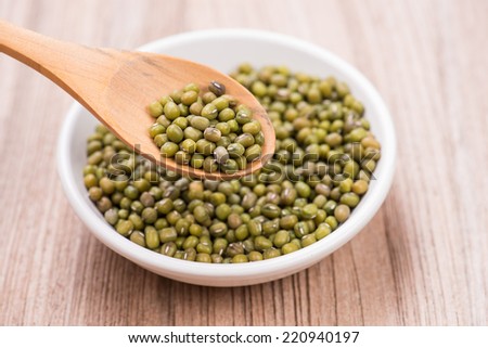 Green mung beans in wooden spoon with ceramic bowl