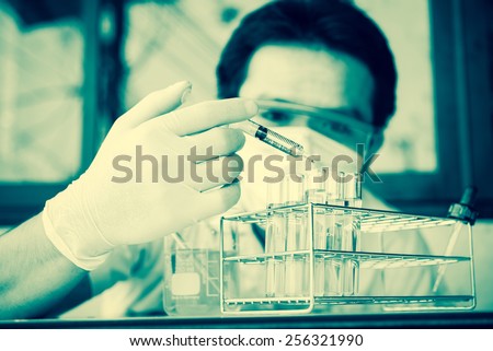 Investigator checking test tubes. Man wears protective goggles ; vintage filtered style
