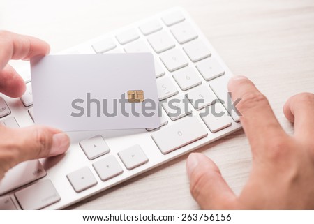 hand holding a white credit card and typing. On-line shopping on the internet