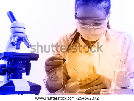 female medical or scientific researcher or woman doctor looking at a test tube of clear solution in a laboratory with her microscope beside her
