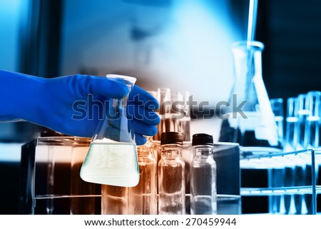 Flask in scientist hand with lab equipment background