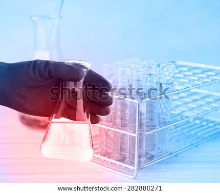 Flask in scientist hand with test tube in rack. Laboratory glassware