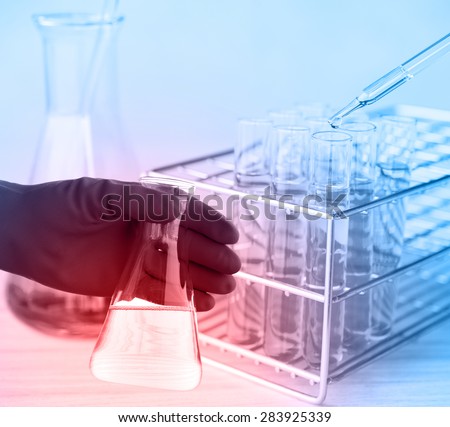 Flask in scientist hand with test tube in rack. Laboratory research, dropping liquid to test tube