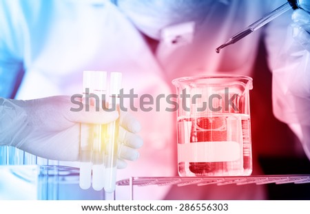 scientist  dropping chemical liquid to flask with test tubes in scientist hand