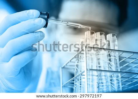 Laboratory pipette with drop of liquid over glass test tubes for an experiment in a science research lab .Man wears protective goggles