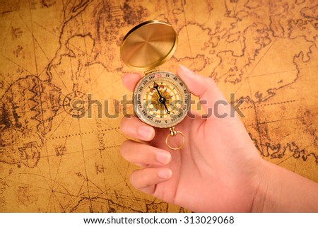 Close up of the hand holding a vintage compass over a vintage map