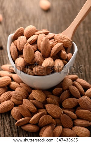almonds in a white ceramic bowl with wood spoon on grained wood background