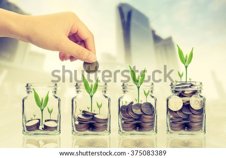 Hand putting money coins and seed in clear bottle on cityscape photo blurred cityscape background,Business investment growth concept