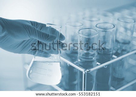 Flask in scientist hand with dropping chemical liquid to test tubes, science and medical research and development concept