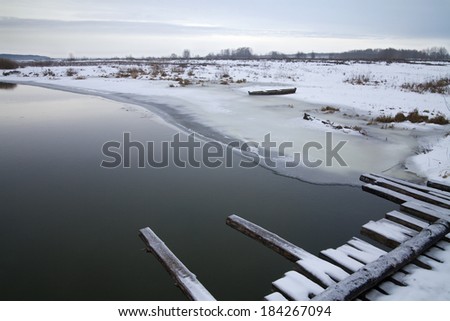 Bank of the river covered with snow and a wooden boat