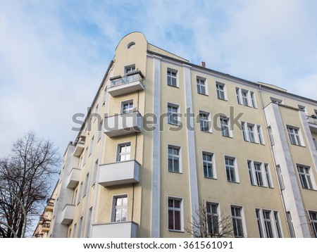 Low Angle Architectural Exterior View of Modern Yellow Low Rise Residential Apartment Building with Small Balconies in Neighborhood with Bare Trees, Blue Sky and Clouds