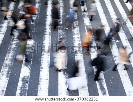 Group of pedestrians crossing the street at a zebra crossing with motion blur to the people and focus to the markings on the road, high angle view
