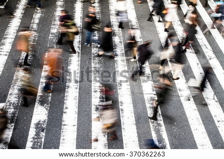 View from above of a crowd of pedestrians on a zebra crossing with motion blur to the walking people and focus to the stripes on the asphalt