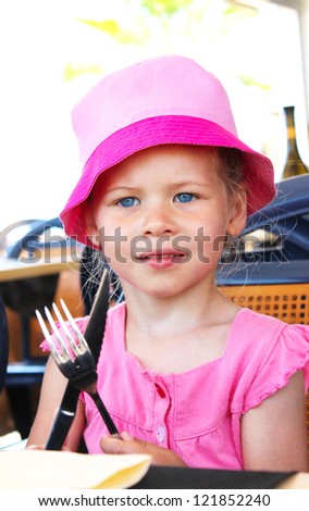 little girl sitting at table holding fork and knife outdoor