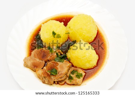Meat with potato dumplings in dark sauce on white plate