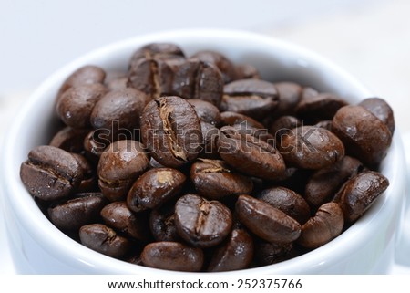 Coffee cup filled with coffee beans. Very shallow focus on coffee beans in cup.
