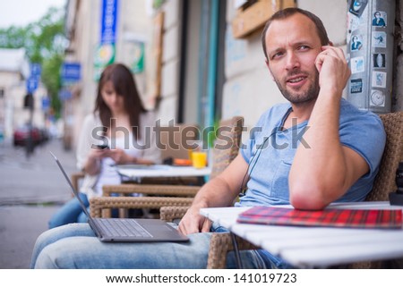 Woman with cell phone and the man with laptop and mobile  phone sitting in a cafe.  Secluded alley in a background.