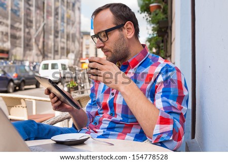 Man with tablet pc in cafe. He is drinking coffee.