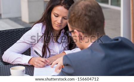Businessman and businesswomen having a meeting in cafe. She is signing a contract.