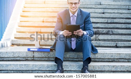 Businessman using electronic tablet pc. He is sitting on a stairs.