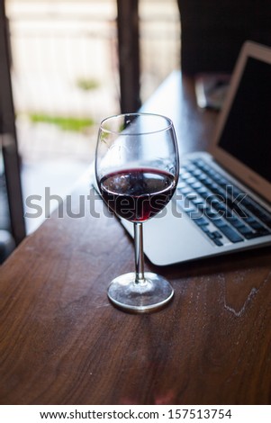 Wine glass with red wine and laptop computer.