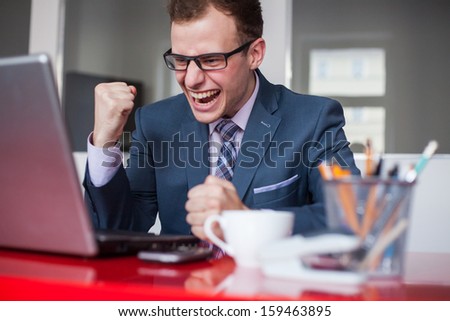 Young happy businessman with laptop computer in office. Expression of emotions.