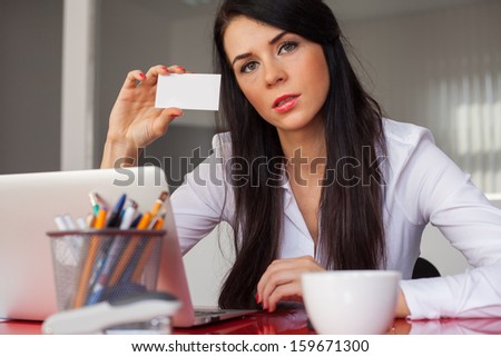 Young cheerful businesswoman holding white business card. She is sitting in his office.