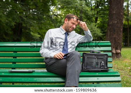 Businessman sitting on a bench with tablet pc. He is full of negative emotion.