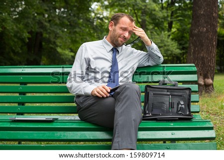 Businessman sitting on a bench with tablet pc. He is full of negative emotion.