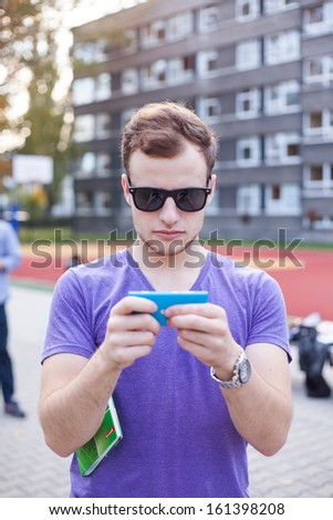 Portrait of a handsome young man posing outdoor at playing field background with mobile phone.