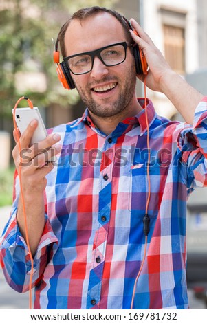 Adult man relaxing with headphones, listening to music. Orange fashionable headphones. He is dressed in shirts Checked. Outdoor