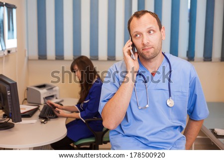Female doctor working on his computer,male doctor working with mobile phone in the office. They are wearing blue smock, (surgeon uniform)