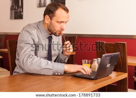 Handsome man sitting alone in restaurant with laptop computer and eating traditional English breakfast. Fried eggs, sausages, beans and bacon