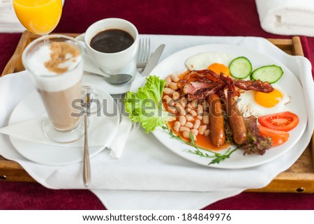 Photo of tray with english breakfast food on the bed inside a bedroom