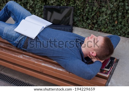 Student rests with a book on wooden bench in the summer. No stress
