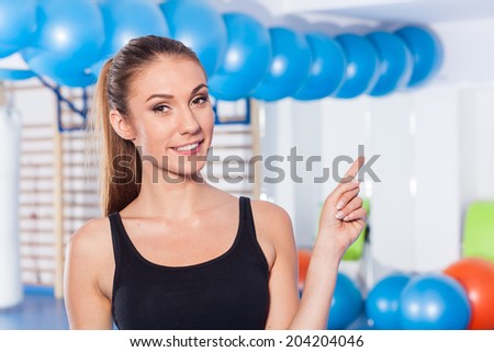 Beautiful happy young woman in gym. Gym shot. Crossfit hall. She is pointing copy space