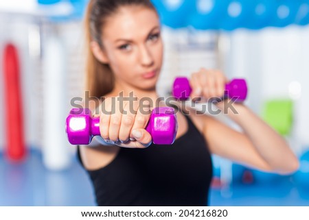 Portrait of a young pretty woman holding weights (dumbbell) and doing fitness indor. Crossfit hall. Gym shot. Selective focus
