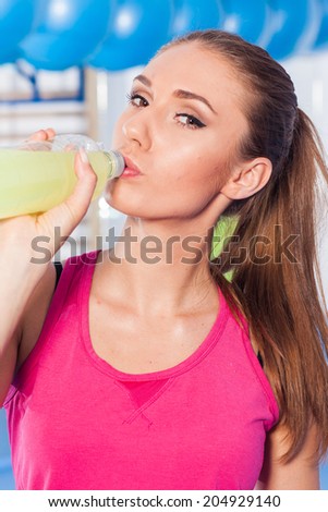 Young girl drinking isotonic drink, gym. Full of positive emotion