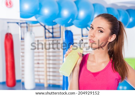 Young girl drinking isotonic drink, gym.