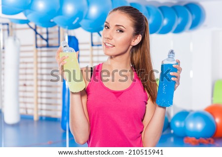 Young girl with two isotonic drink (yellow, blue), gym. She is considering which one to choose